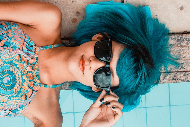Ležiaca žena s modrými vlasmi vo farebnom tričku a v slnečných okuliaroch na očiach.jpg